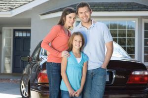 family smiling at camera in front of a car